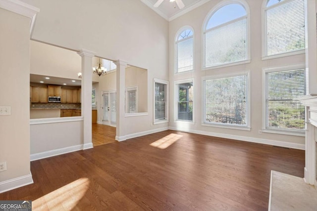 unfurnished living room with a towering ceiling, dark hardwood / wood-style floors, plenty of natural light, and crown molding