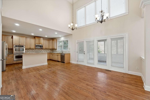 kitchen featuring stainless steel appliances, an inviting chandelier, a towering ceiling, light hardwood / wood-style floors, and decorative light fixtures