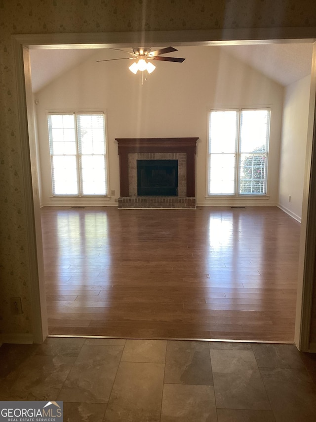 unfurnished living room featuring vaulted ceiling, a brick fireplace, dark hardwood / wood-style floors, and a wealth of natural light