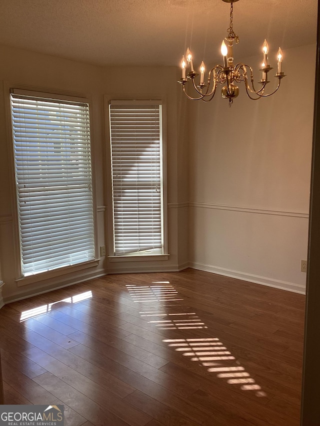 unfurnished room with an inviting chandelier, a textured ceiling, and dark hardwood / wood-style floors