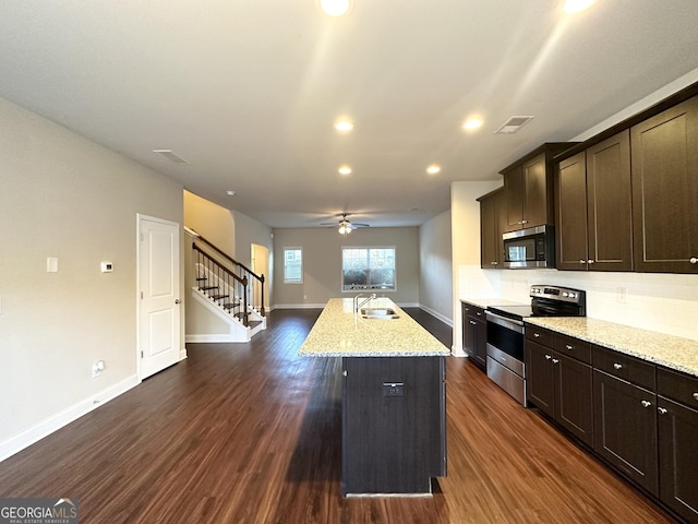 kitchen featuring a kitchen island with sink, dark hardwood / wood-style flooring, light stone counters, and appliances with stainless steel finishes