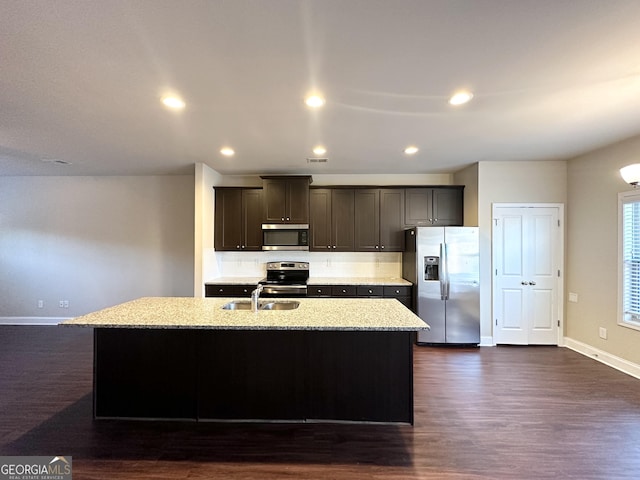 kitchen with light stone counters, stainless steel appliances, sink, dark hardwood / wood-style floors, and an island with sink