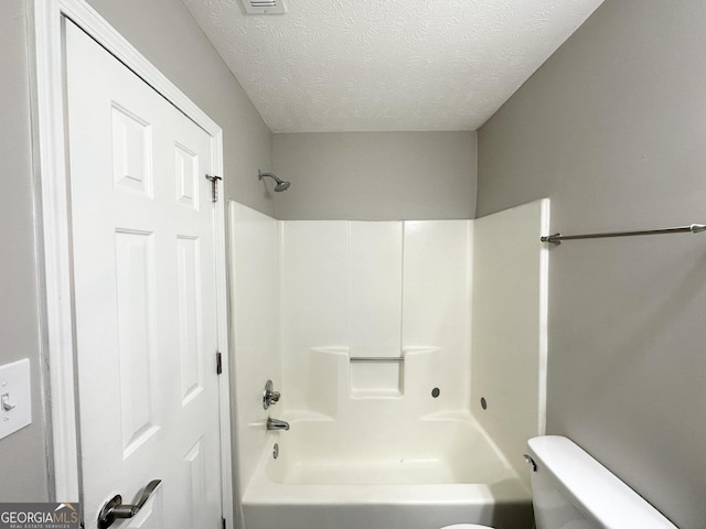 bathroom featuring toilet, a textured ceiling, and bathing tub / shower combination