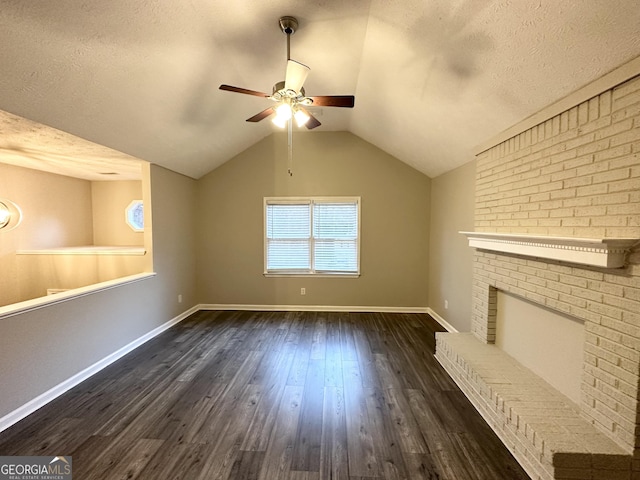 unfurnished living room with ceiling fan, a brick fireplace, dark hardwood / wood-style flooring, a textured ceiling, and vaulted ceiling