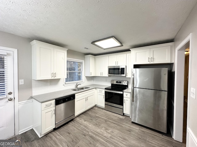 kitchen with sink, light hardwood / wood-style floors, a textured ceiling, white cabinets, and appliances with stainless steel finishes