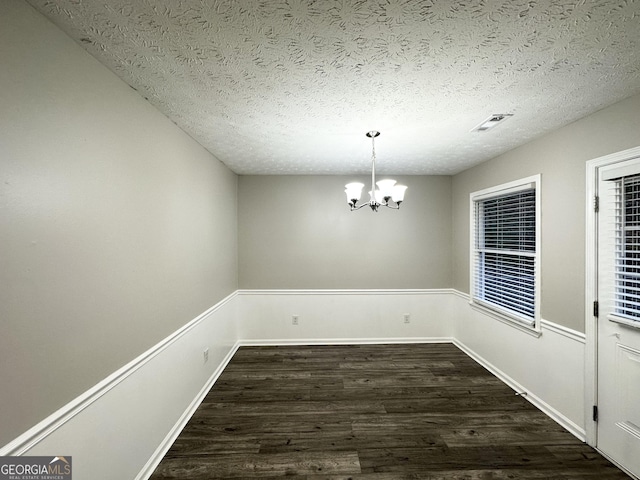 unfurnished dining area featuring a textured ceiling, dark hardwood / wood-style floors, and an inviting chandelier