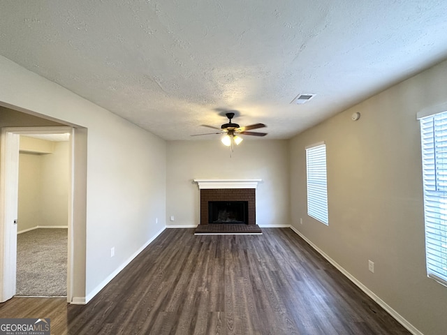 unfurnished living room with a textured ceiling, a brick fireplace, ceiling fan, and dark wood-type flooring