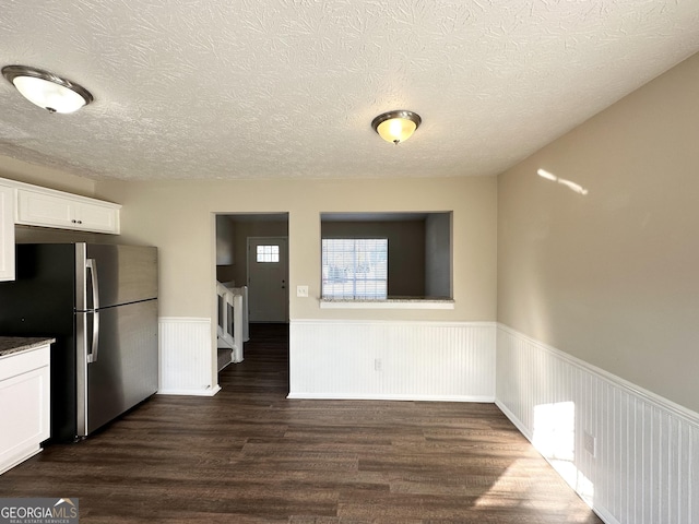 kitchen with a textured ceiling, stainless steel fridge, white cabinetry, and dark wood-type flooring