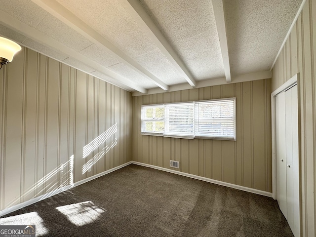 unfurnished room with wood walls, dark carpet, and beam ceiling