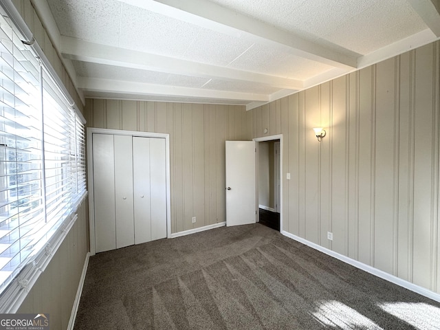 unfurnished bedroom with beam ceiling, wood walls, a closet, and dark carpet