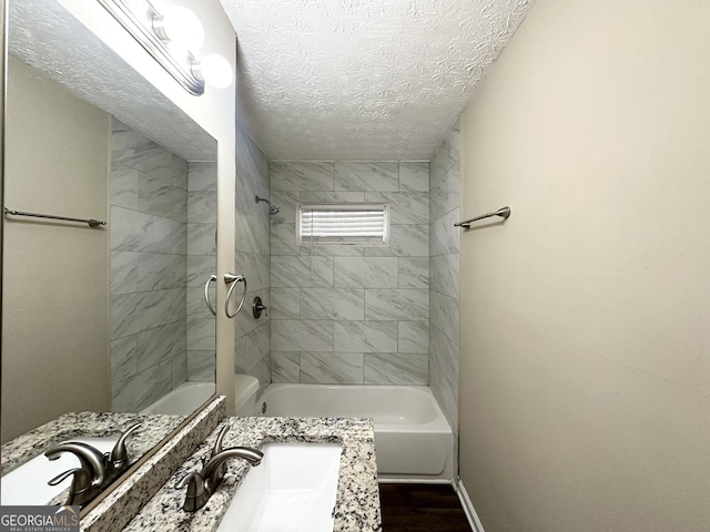 bathroom with a textured ceiling, vanity, wood-type flooring, and tiled shower / bath