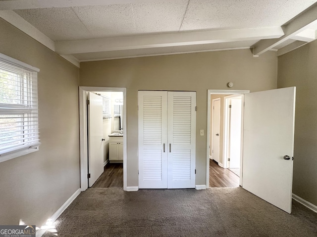 unfurnished bedroom with ensuite bathroom, lofted ceiling with beams, and dark colored carpet