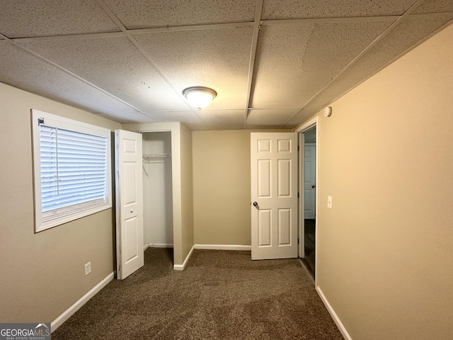 unfurnished bedroom featuring a closet, a drop ceiling, and dark colored carpet