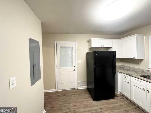 kitchen featuring black refrigerator, light stone countertops, white cabinetry, and electric panel