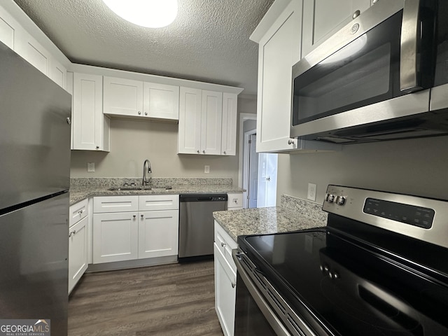 kitchen with appliances with stainless steel finishes, a textured ceiling, dark hardwood / wood-style floors, and white cabinetry