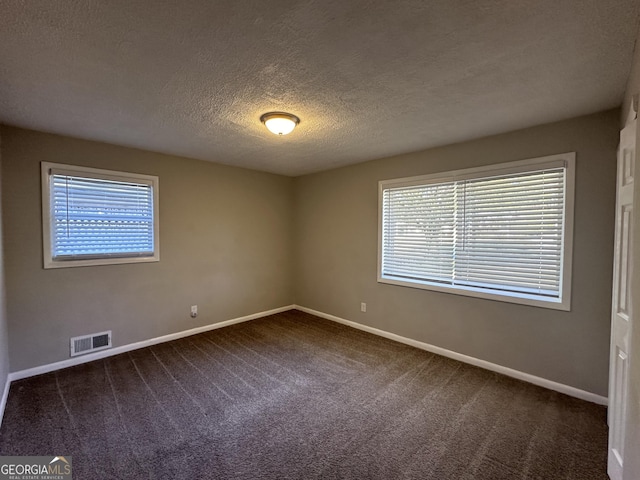 spare room with a textured ceiling, dark carpet, and a healthy amount of sunlight