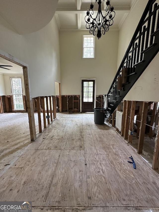 unfurnished living room featuring beamed ceiling, a towering ceiling, a chandelier, and crown molding