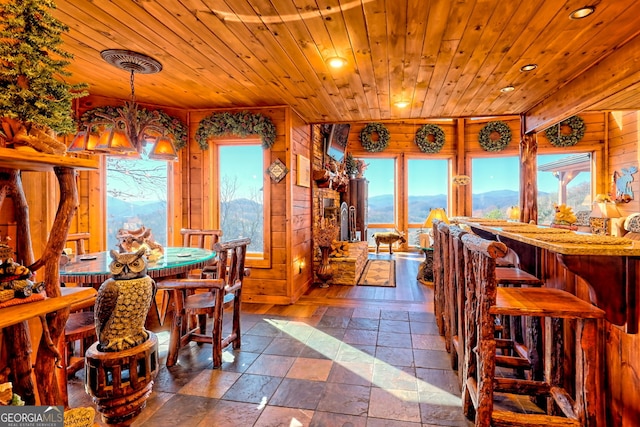 dining space featuring a mountain view, a healthy amount of sunlight, wood ceiling, and wooden walls