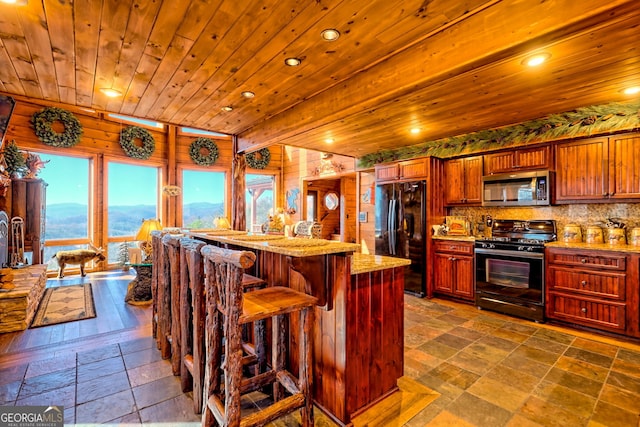 kitchen featuring wooden ceiling, tasteful backsplash, wood walls, a kitchen bar, and black appliances