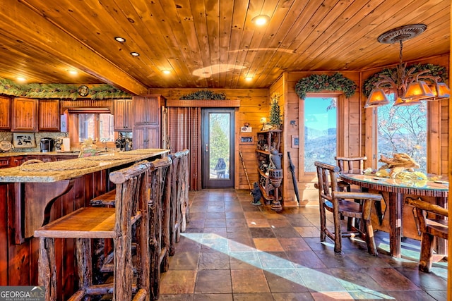 kitchen featuring wood walls, decorative backsplash, decorative light fixtures, light stone counters, and wood ceiling