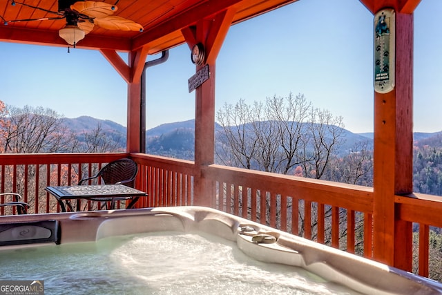 wooden terrace with a mountain view, ceiling fan, and a hot tub