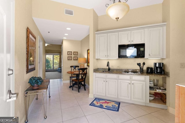 kitchen featuring light tile patterned flooring, white cabinetry, dark stone counters, and sink