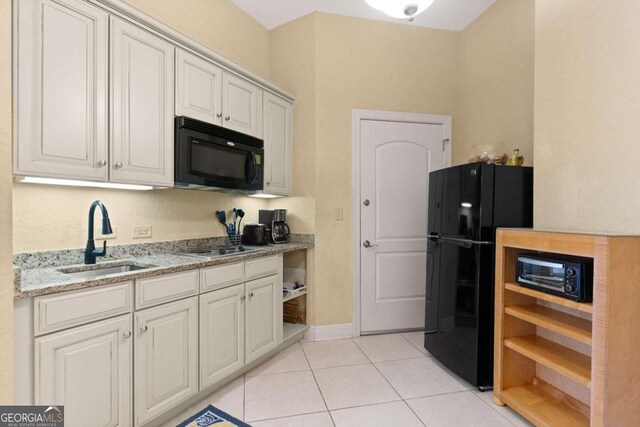 kitchen with light stone counters, sink, black appliances, white cabinetry, and light tile patterned flooring