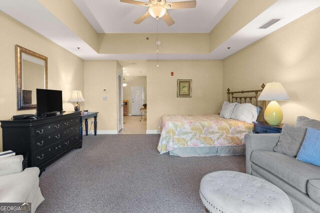 bedroom with a raised ceiling, ceiling fan, and light carpet