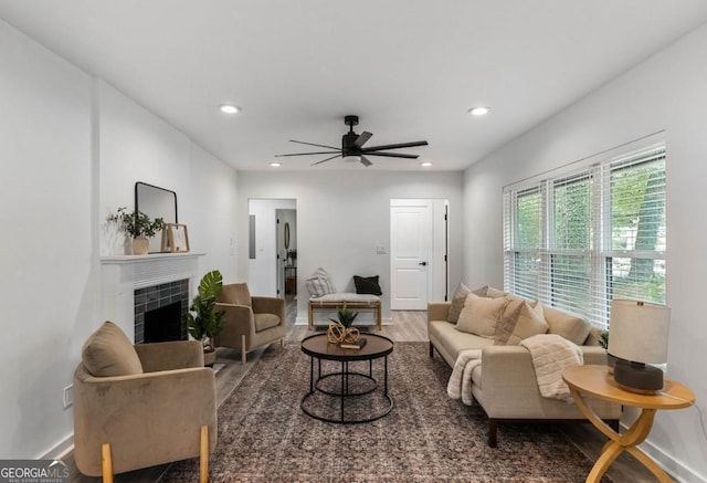 living room featuring a tiled fireplace, ceiling fan, and dark wood-type flooring