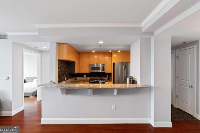 kitchen featuring kitchen peninsula, appliances with stainless steel finishes, backsplash, dark wood-type flooring, and a breakfast bar area