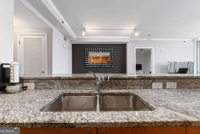 kitchen with light stone countertops, sink, track lighting, and ornamental molding