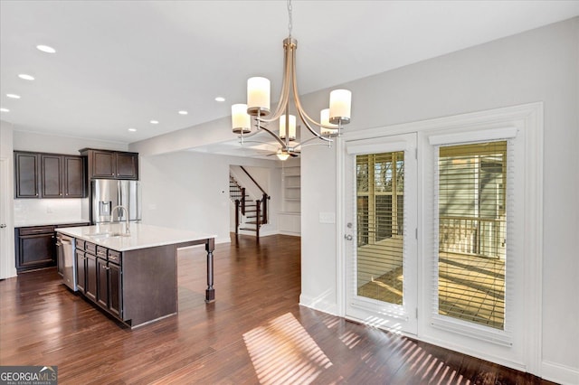 kitchen with pendant lighting, sink, stainless steel appliances, dark wood-type flooring, and a center island with sink