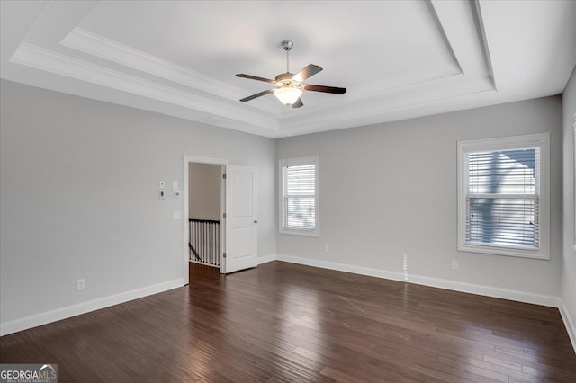 empty room featuring dark wood-type flooring, ceiling fan, ornamental molding, and a raised ceiling