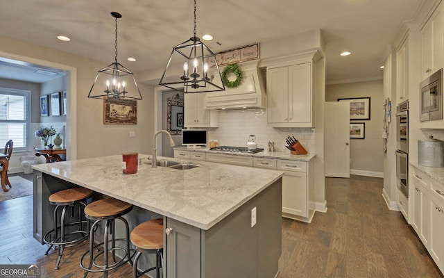 kitchen with sink, light stone countertops, an island with sink, and hanging light fixtures