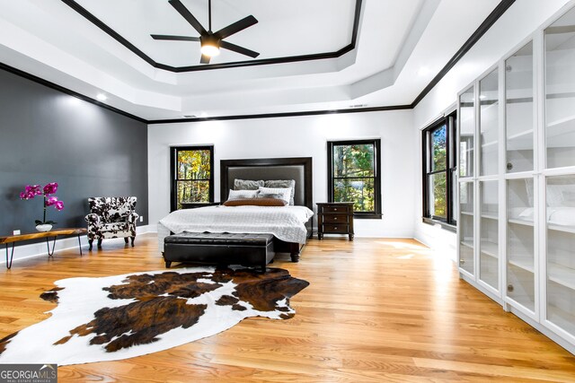 bedroom with a tray ceiling, ceiling fan, ornamental molding, and light wood-type flooring