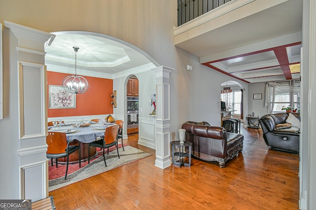 interior space featuring coffered ceiling, crown molding, light wood-type flooring, a notable chandelier, and decorative columns