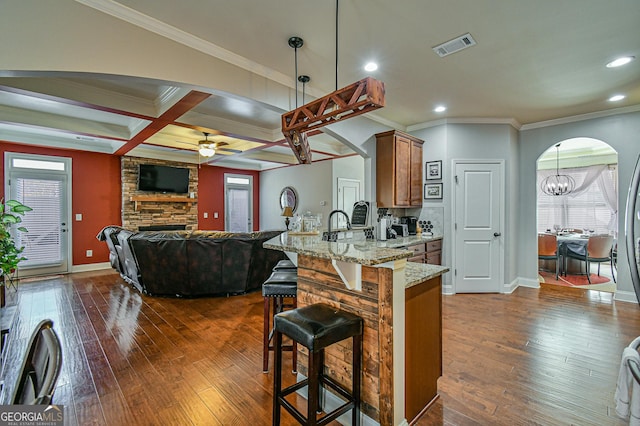 kitchen with light stone countertops, dark hardwood / wood-style flooring, coffered ceiling, ceiling fan with notable chandelier, and decorative light fixtures