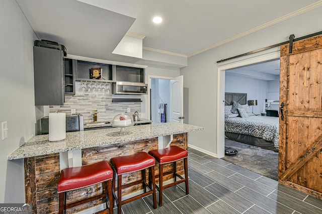 kitchen with light stone countertops, tasteful backsplash, a barn door, kitchen peninsula, and a breakfast bar area