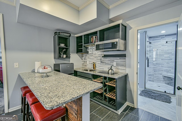 kitchen featuring tasteful backsplash, light stone counters, kitchen peninsula, crown molding, and a breakfast bar area