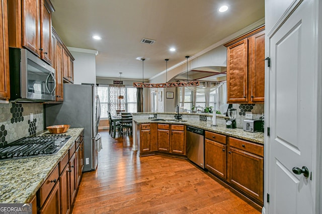 kitchen with kitchen peninsula, ornamental molding, stainless steel appliances, pendant lighting, and hardwood / wood-style flooring