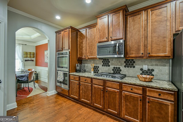 kitchen with light stone countertops, crown molding, decorative backsplash, appliances with stainless steel finishes, and hardwood / wood-style flooring