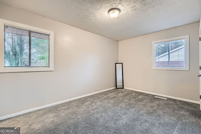 spare room featuring dark colored carpet and a textured ceiling