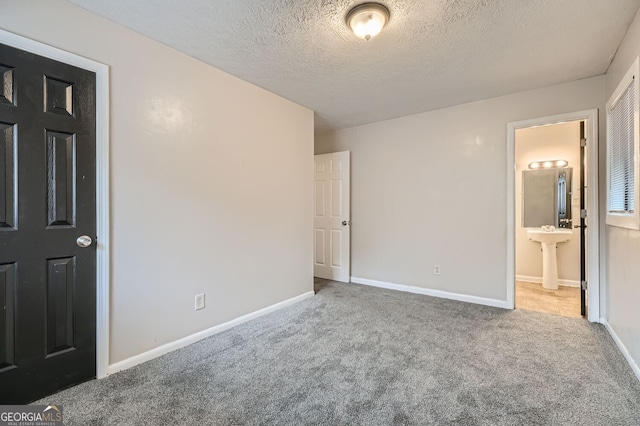 unfurnished bedroom featuring sink, light colored carpet, a textured ceiling, and ensuite bath