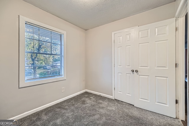 unfurnished bedroom featuring dark carpet, a textured ceiling, and a closet