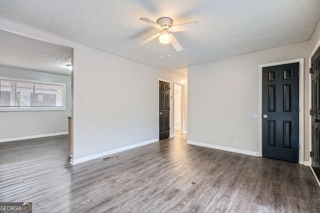 empty room with ceiling fan, dark wood-type flooring, and a textured ceiling