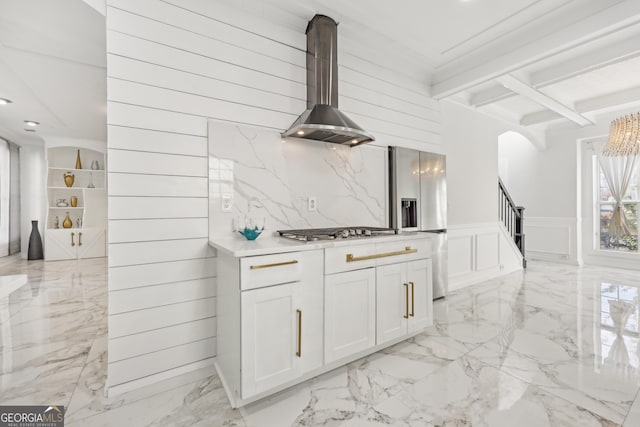 kitchen with white cabinets, wall chimney range hood, ornamental molding, beamed ceiling, and stainless steel appliances