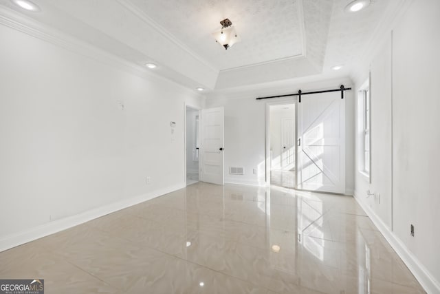 empty room with a textured ceiling, a barn door, a raised ceiling, and ornamental molding