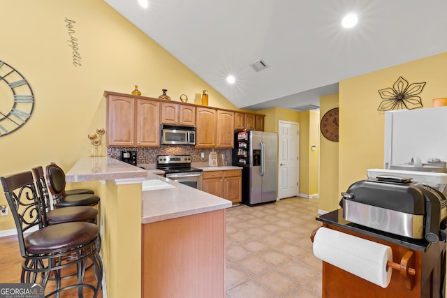 kitchen featuring backsplash, kitchen peninsula, vaulted ceiling, a breakfast bar, and appliances with stainless steel finishes