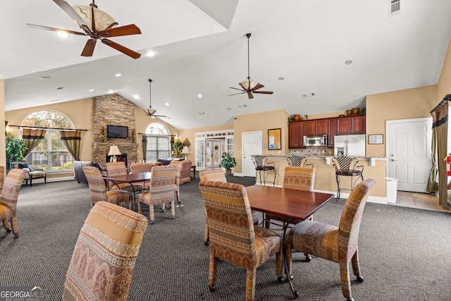 carpeted dining room with a stone fireplace, ceiling fan, and high vaulted ceiling