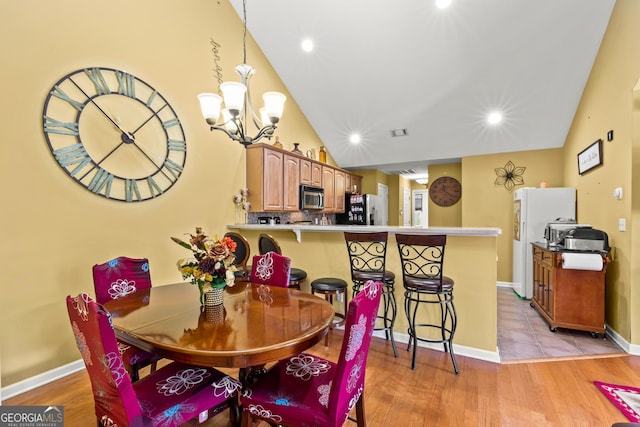 dining room featuring light wood-type flooring, an inviting chandelier, and vaulted ceiling